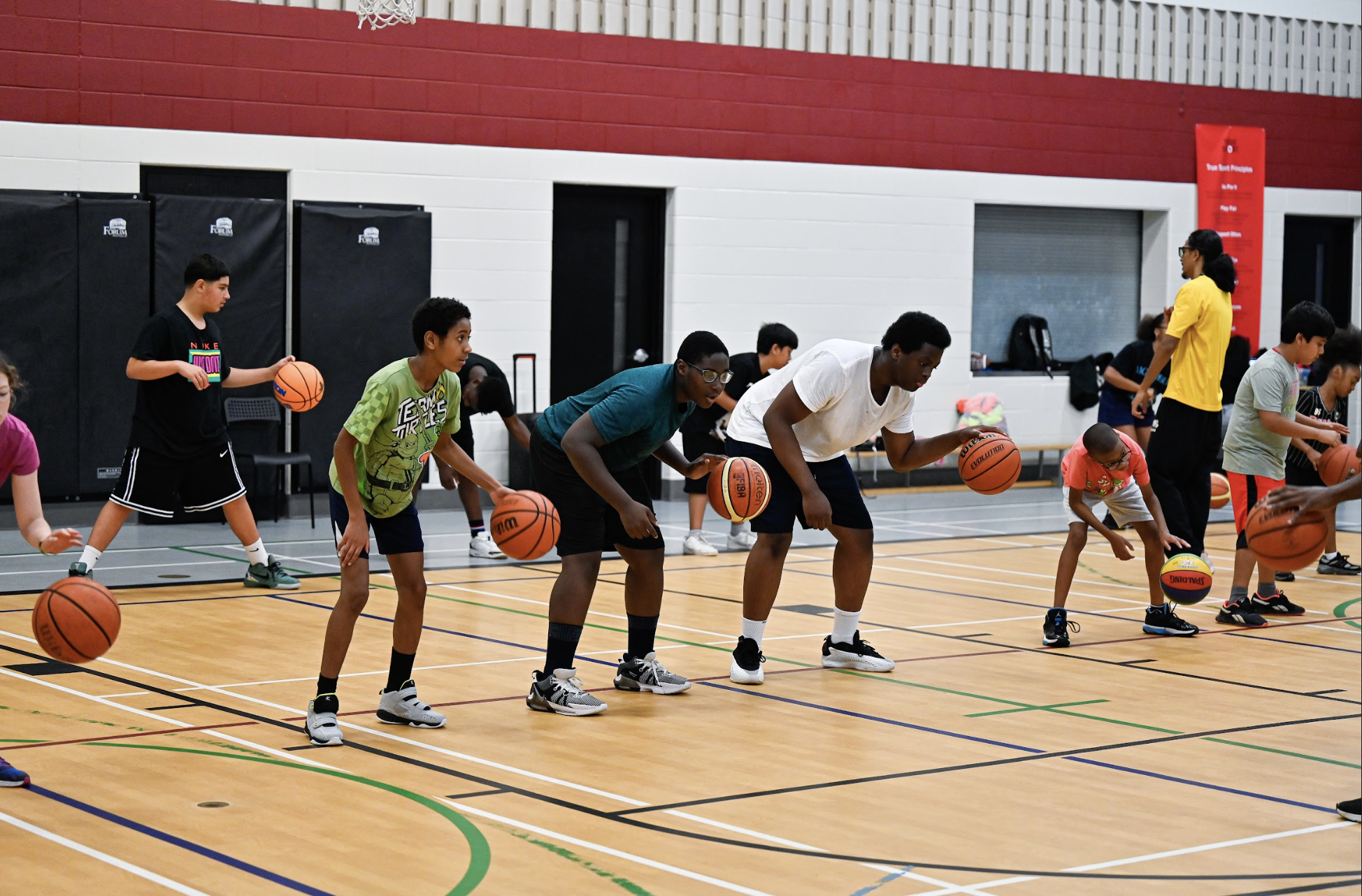A group of campers dribbling basketballs at a school gym